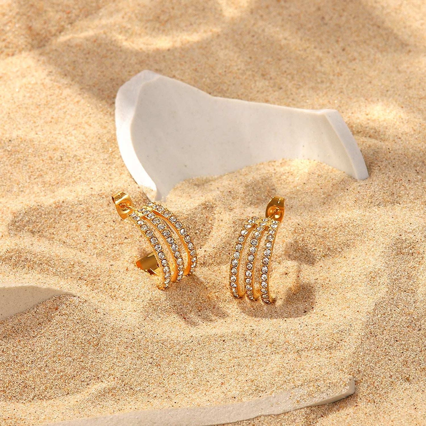 Stainless steel inlaid zircon C-hoop earrings on sand background.