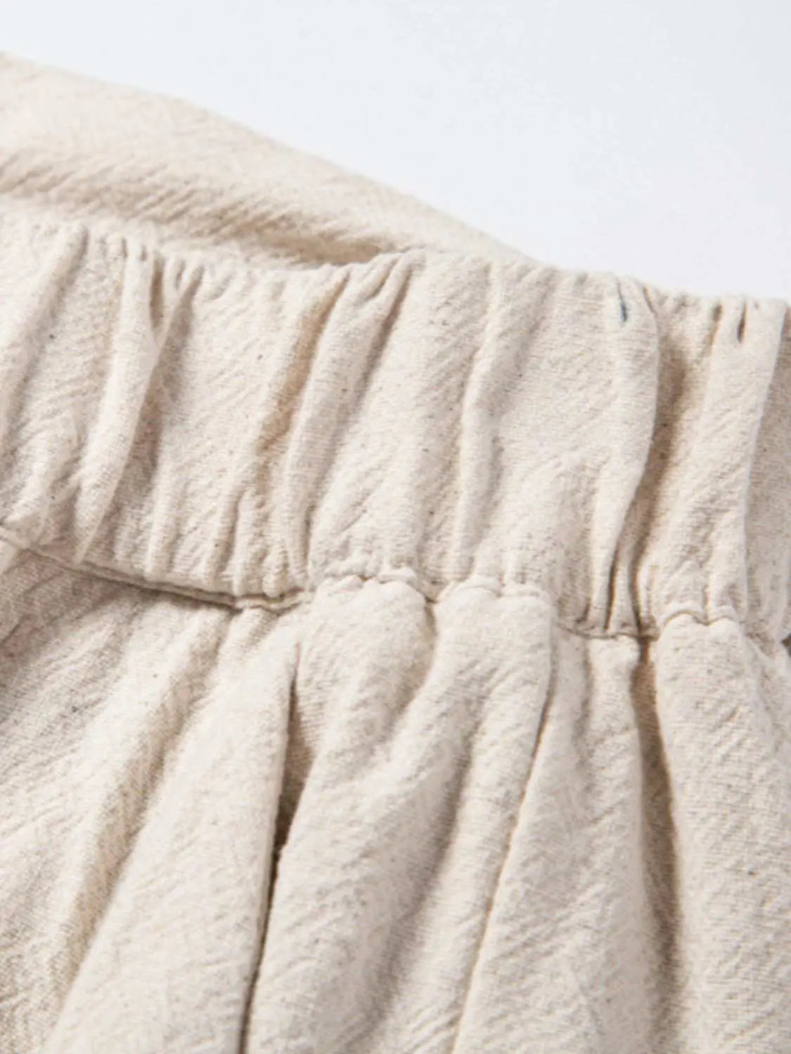 Close-up of elastic waistband on men's drawstring pants in beige fabric.