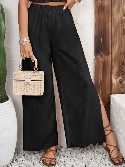 Smocked Surplice cami and wide leg pants set in black with ruffled and slit design, styled with a small wicker handbag and flat sandals.