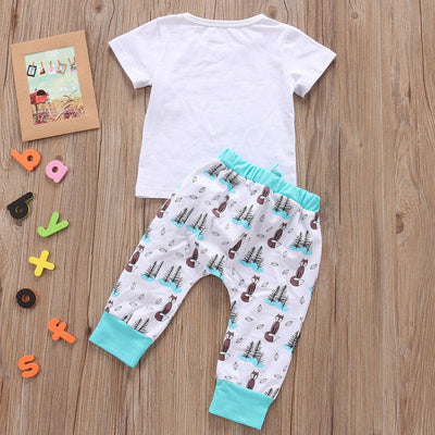 Newborn baby clothes set with white T-shirt and printed pants on a wooden background.