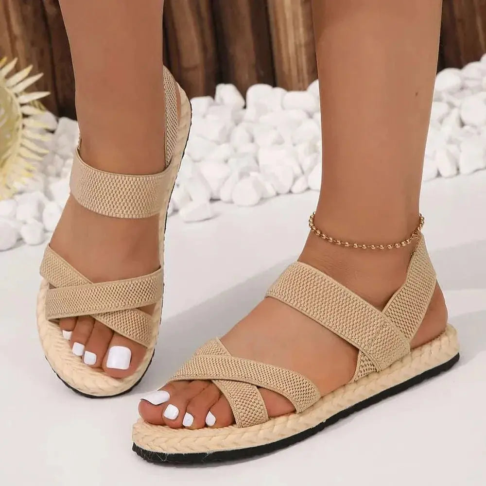 Crisscross open toe flat sandals in beige with rubber and cloth material.