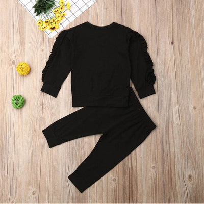 Newborn ruffle jumper 2-piece set with long sleeve top and pants in black, displayed on a wooden background with decorative elements.