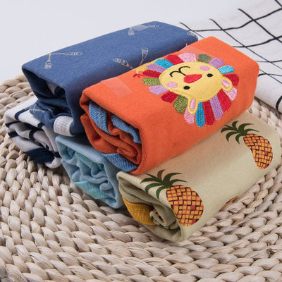Baby Triangle Harmony Set - Colorful folded cotton baby clothes on a woven surface, featuring playful designs including a lion and pineapples.