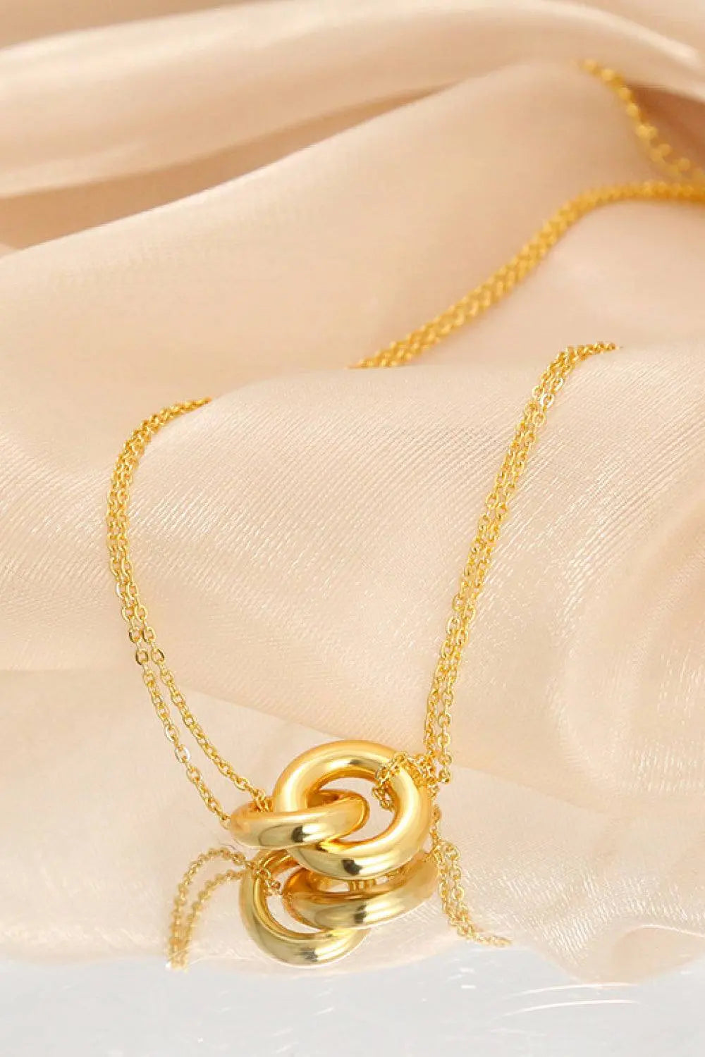 Linked ring pendant chain necklace in brass, elegant and simple design on a light fabric background.