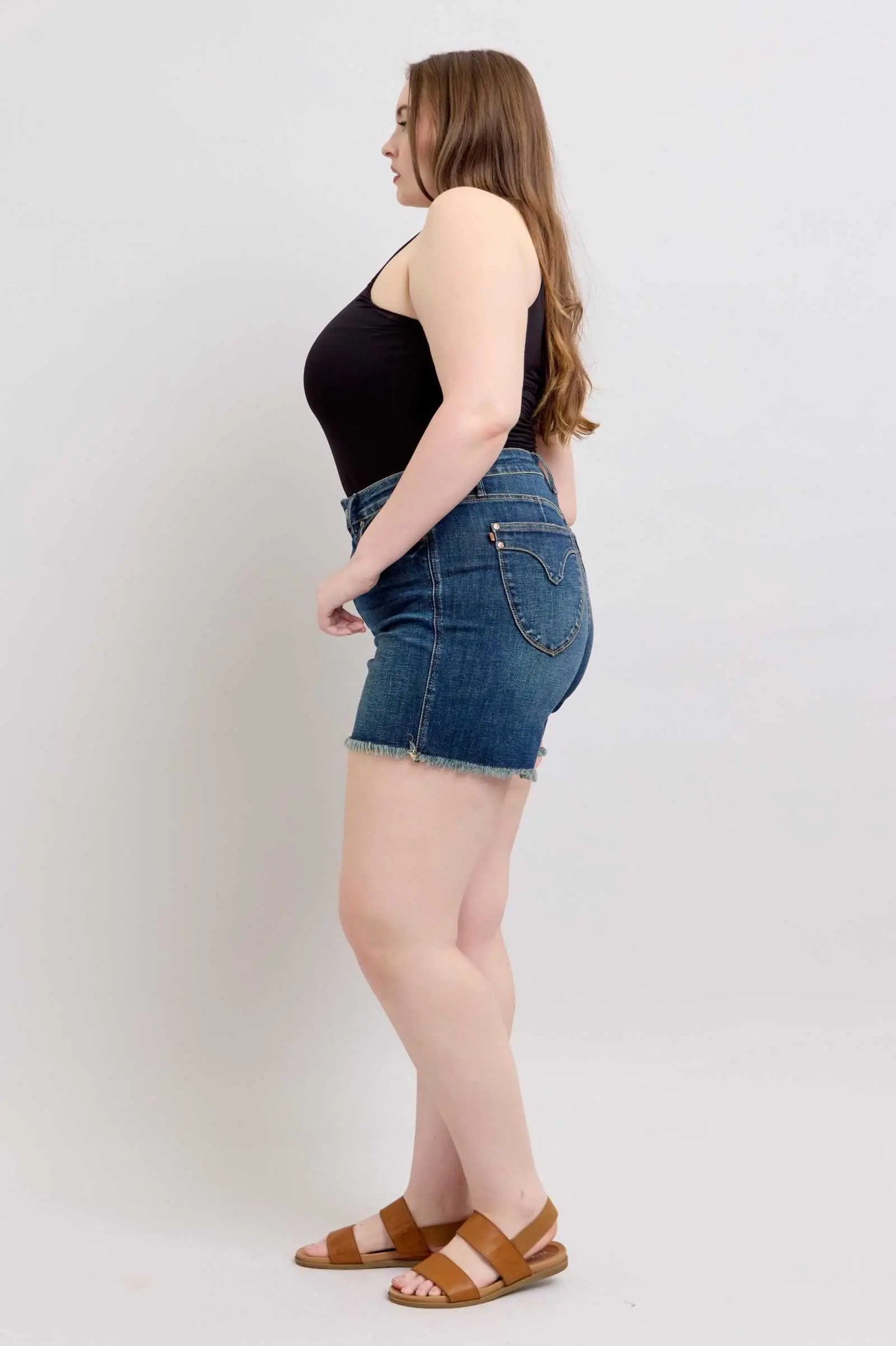 Judy Blue Tummy Control fray hem denim shorts with shield back pockets worn by model.