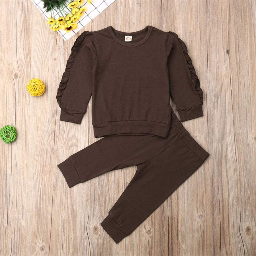 Newborn ruffle jumper 2-piece set with long sleeve top and pants in brown, displayed on a wooden surface with decorative items.