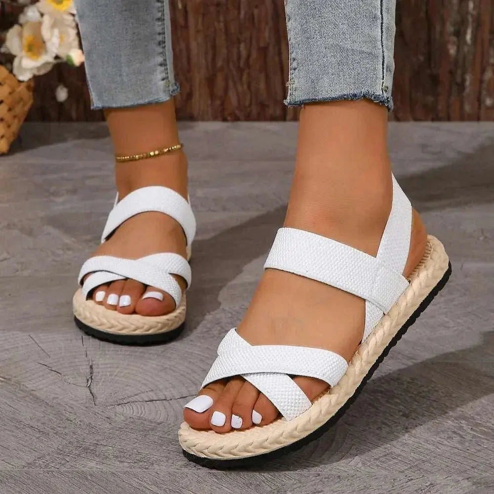 Crisscross open toe flat sandals in white with rubber and cloth material, worn with jeans.
