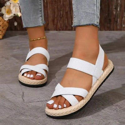 Crisscross open toe flat sandals in white with rubber and cloth material, worn with jeans.