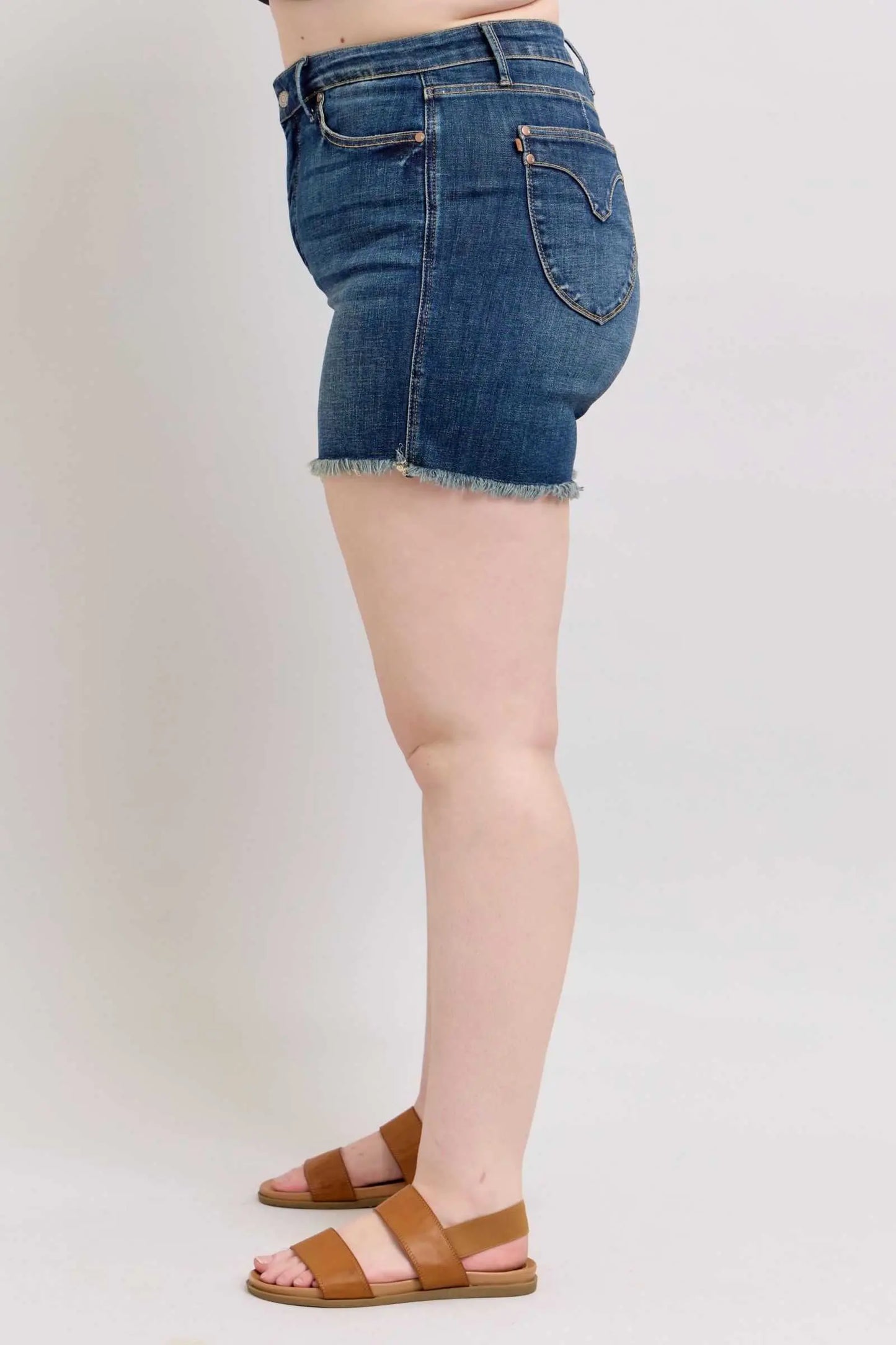 Judy Blue tummy control denim shorts with fray hem and shield back pockets, shown in side view.