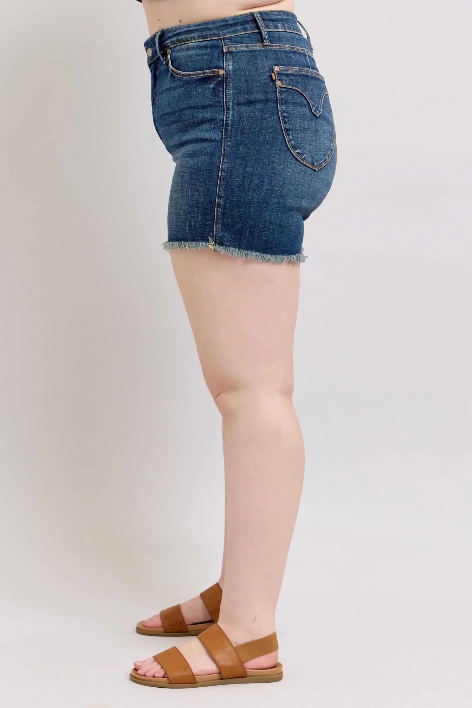 Judy Blue tummy control denim shorts with fray hem and shield back pockets, shown in side view.