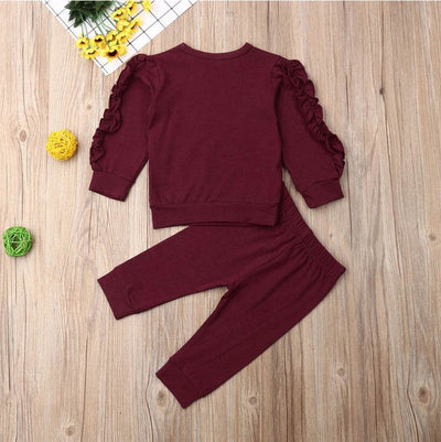 Newborn ruffle jumper 2-piece set in maroon, featuring a long sleeve top with ruffled shoulders and matching pants on a wooden background.