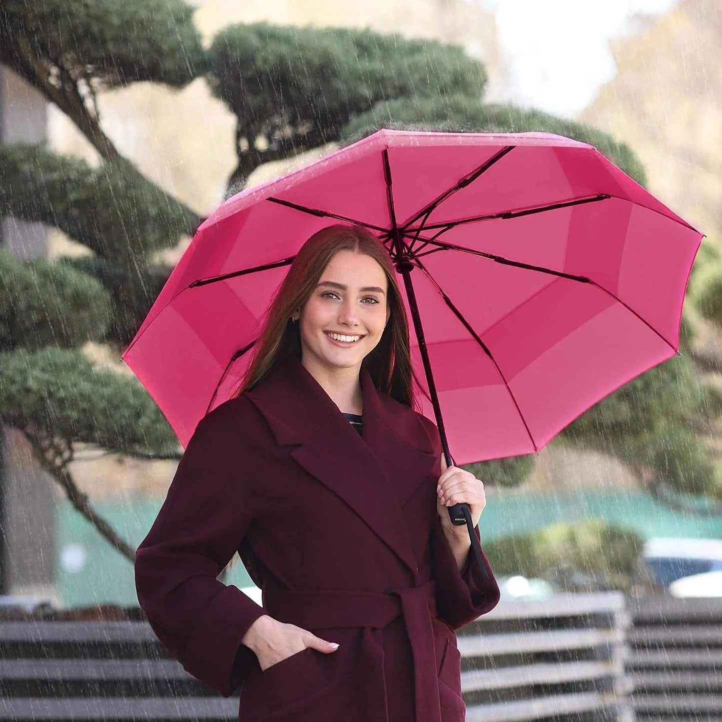Woman holding a pink Repel Umbrella Windproof in the rain, showcasing its durability and compact design.