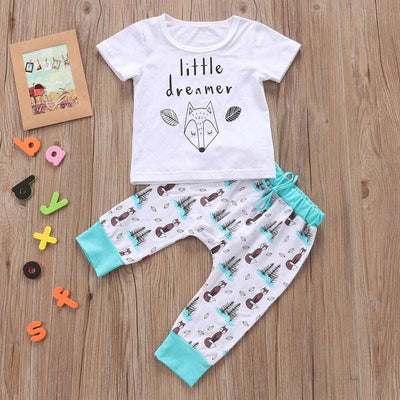 Newborn baby clothes set with white "little dreamer" T-shirt and patterned pants on wooden background.