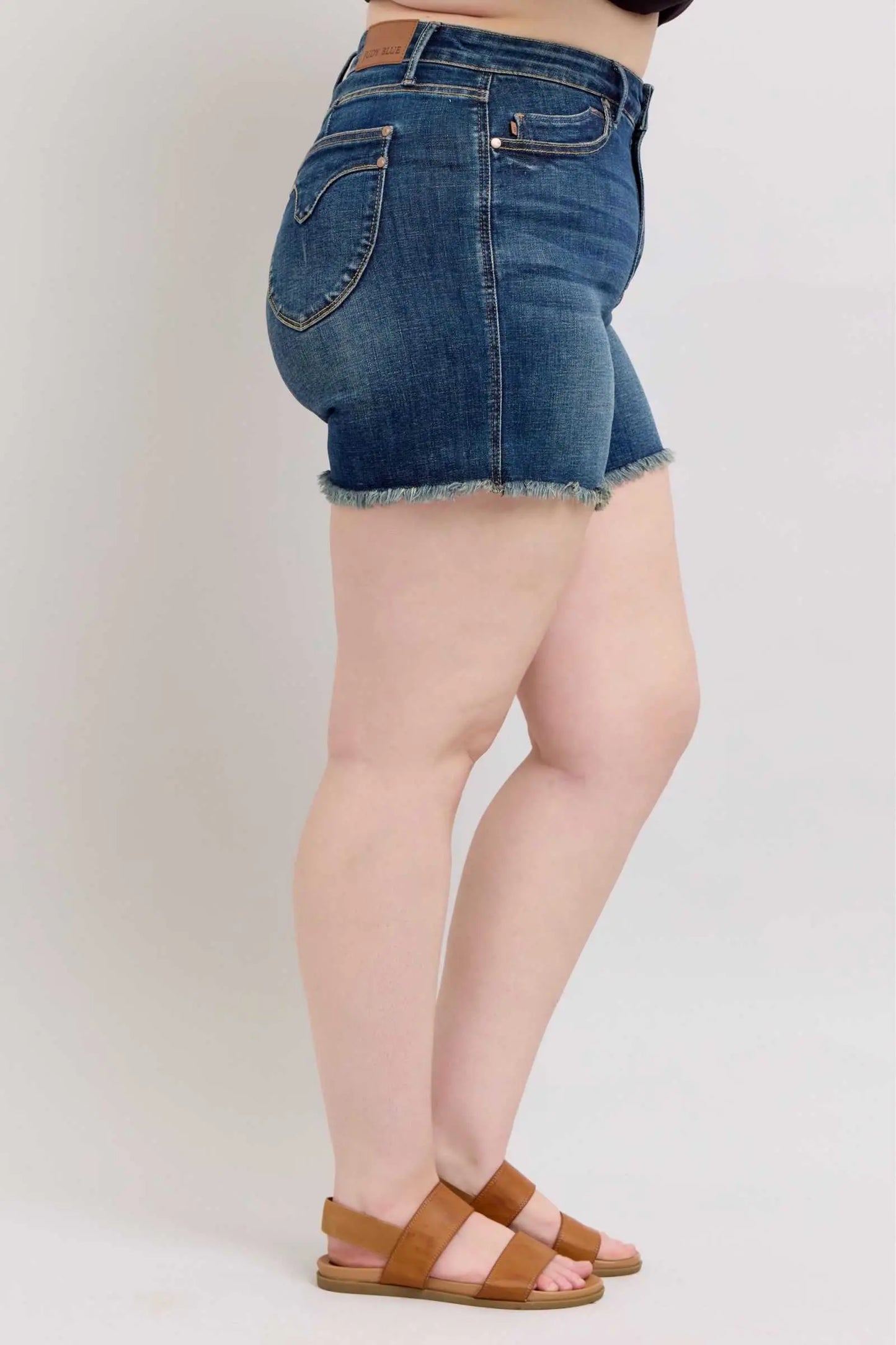 Judy Blue Tummy Control denim shorts with fray hem and shield back pockets, side view.