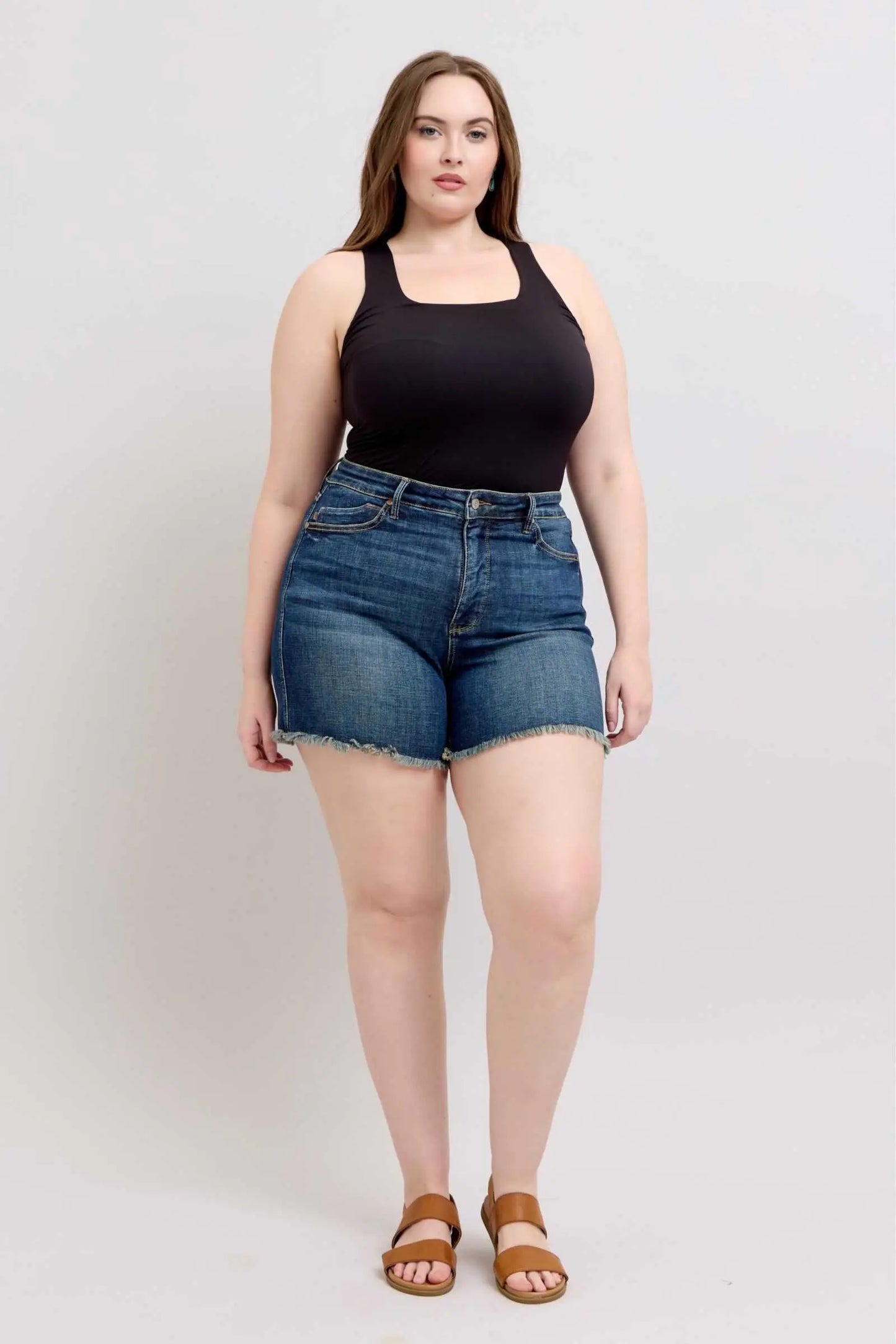 Judy Blue Tummy Control fray hem denim shorts with shield back pockets worn by a model.
