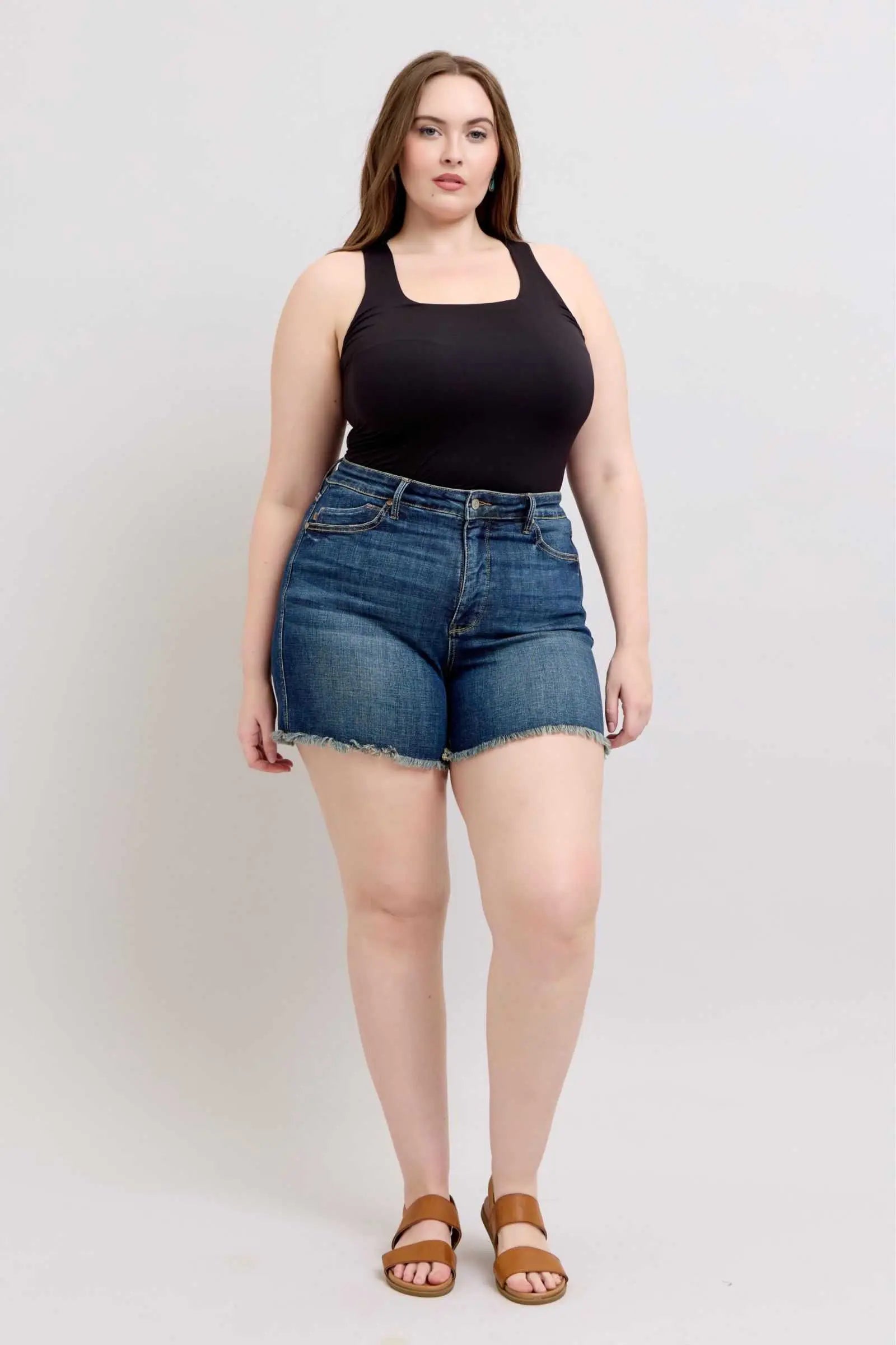 Judy Blue Tummy Control fray hem denim shorts with shield back pockets worn by a model.