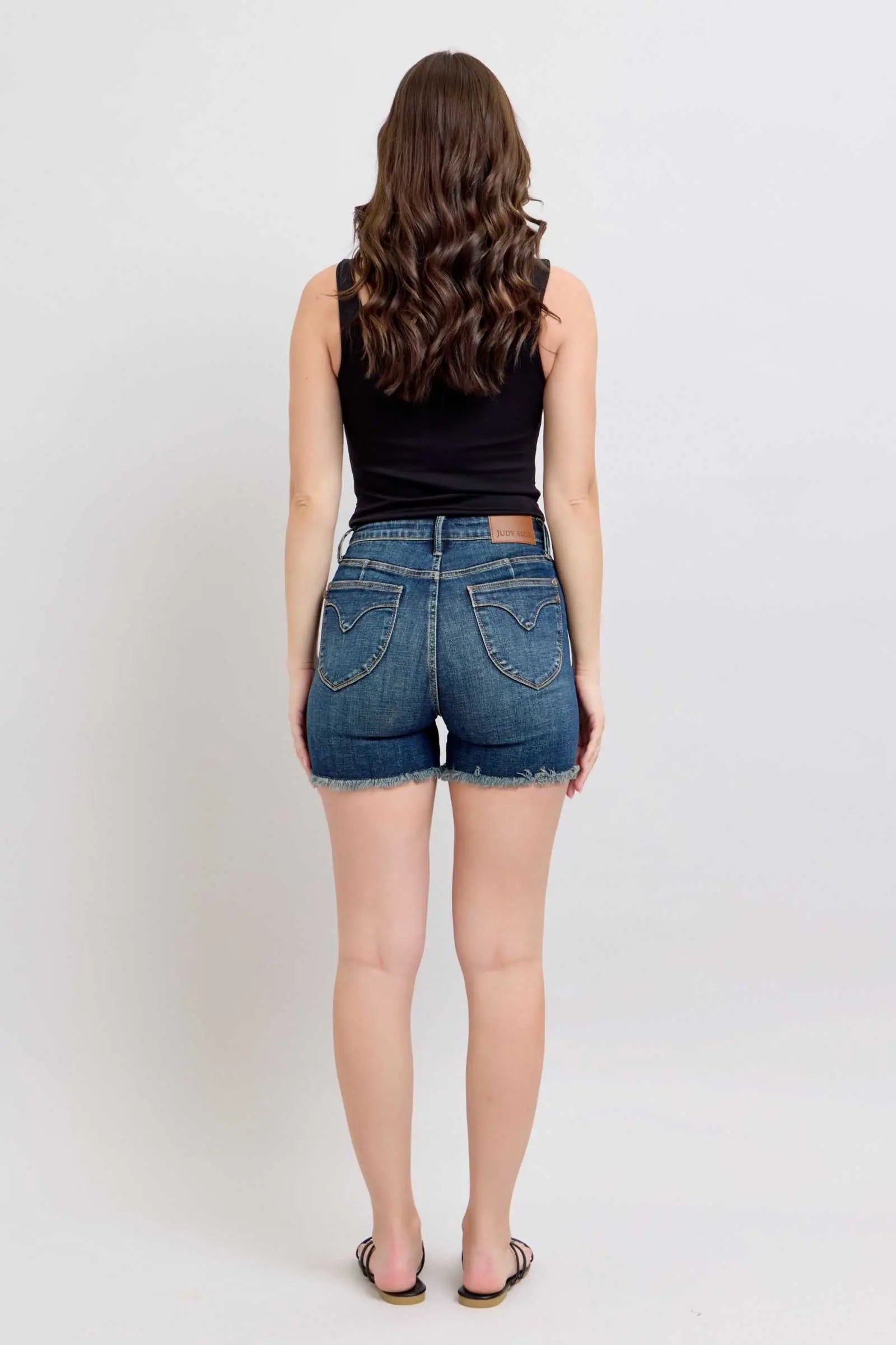Judy Blue Tummy Control denim shorts with fray hem and shield back pockets, rear view.