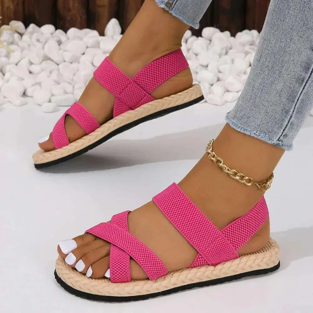 Crisscross open toe flat sandals with pink straps and braided sole on a woman's feet.