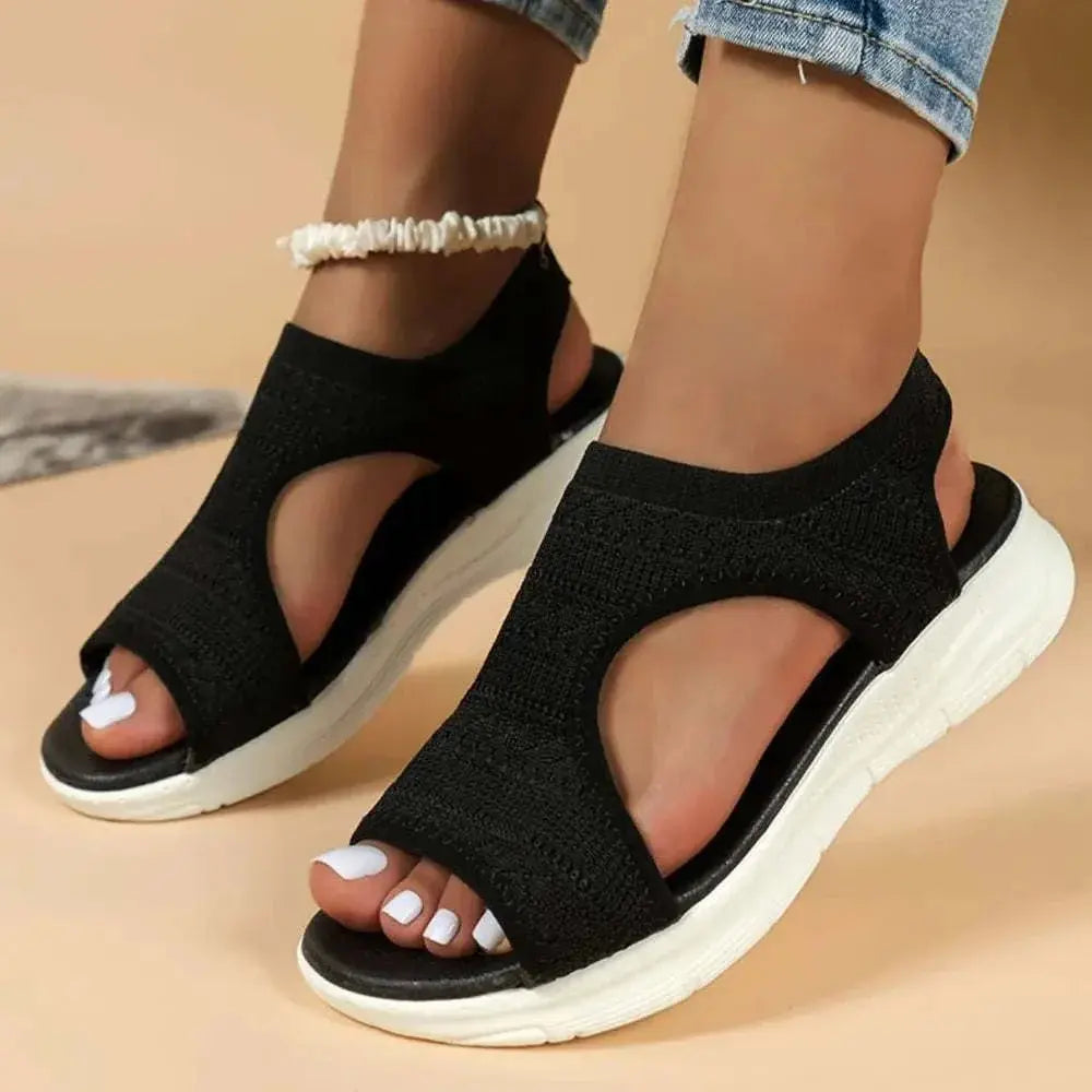 Peep toe solid color sandals in black with flat heel design, featuring rubber and cloth material.