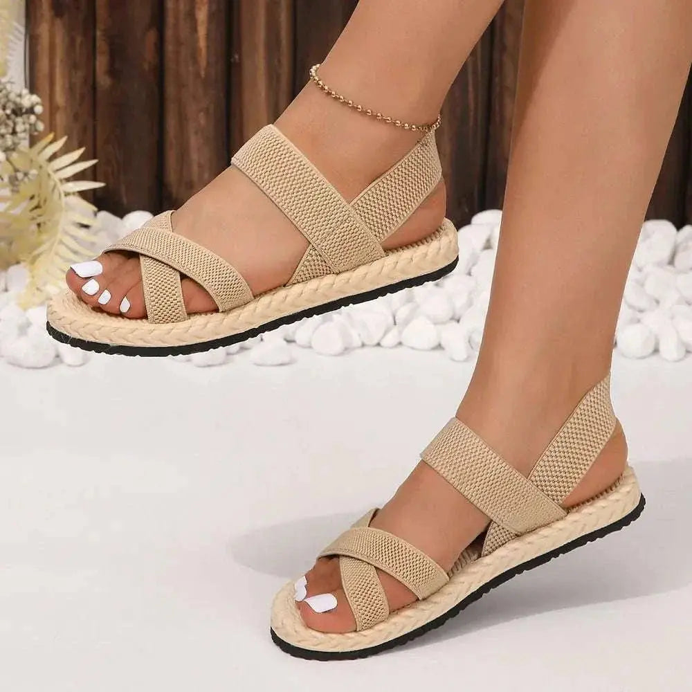 Crisscross open toe flat sandals with rubber and cloth material, shown on feet, featuring a comfortable design ideal for summer.