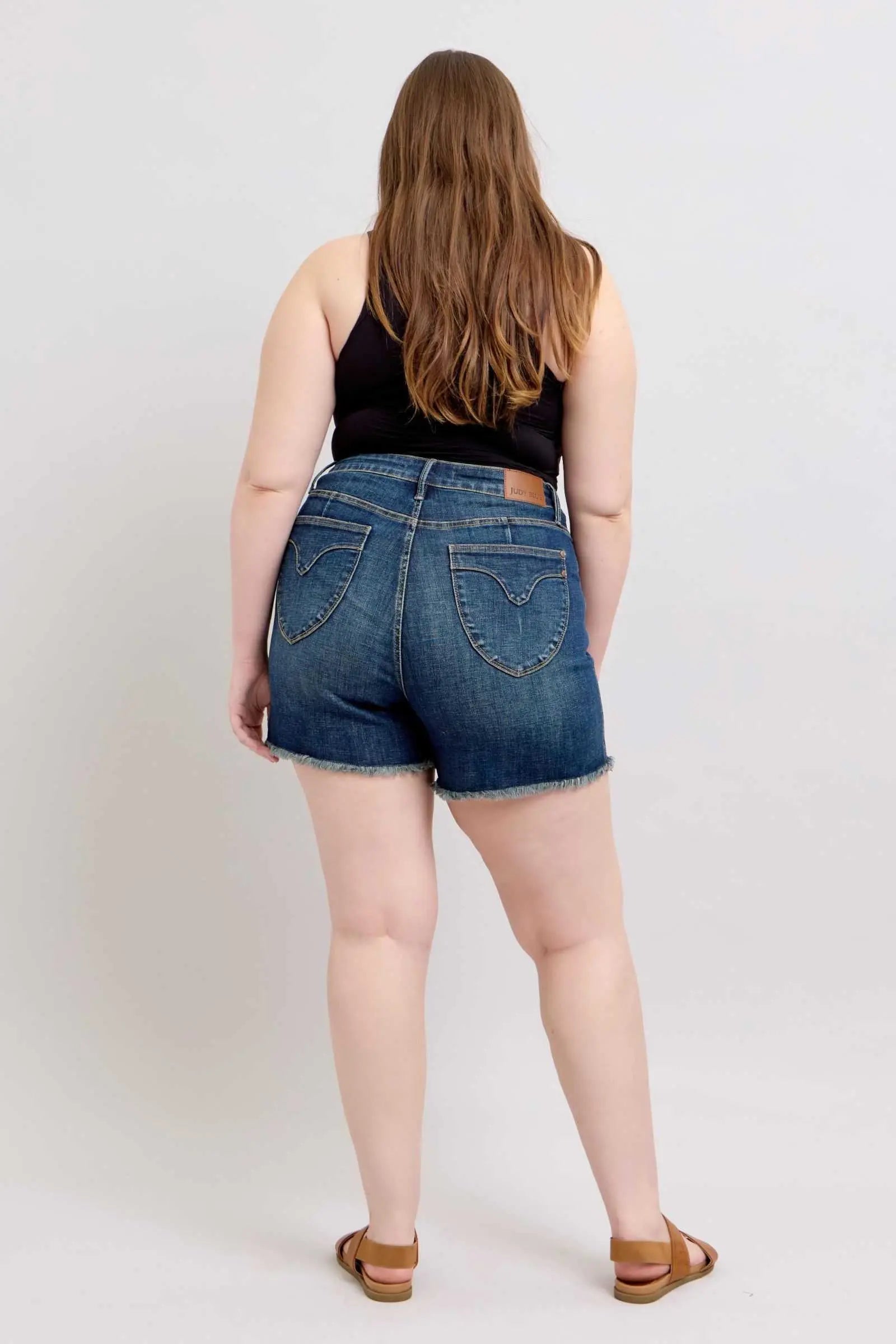 Judy Blue Tummy Control fray hem denim shorts with shield back pockets, shown from the back, featuring a slimming design and trendy details.